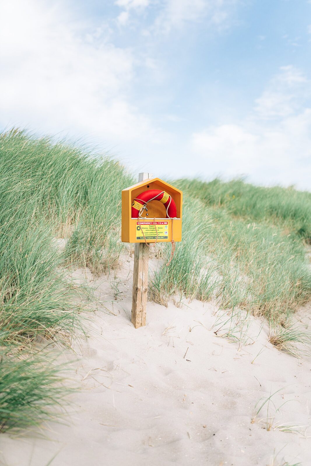 Pop of red and yellow and orange life-saver against soft, muted tones of greens and sand and sky on the iconic Inch Beach, perfect for luxury home decor wall art.